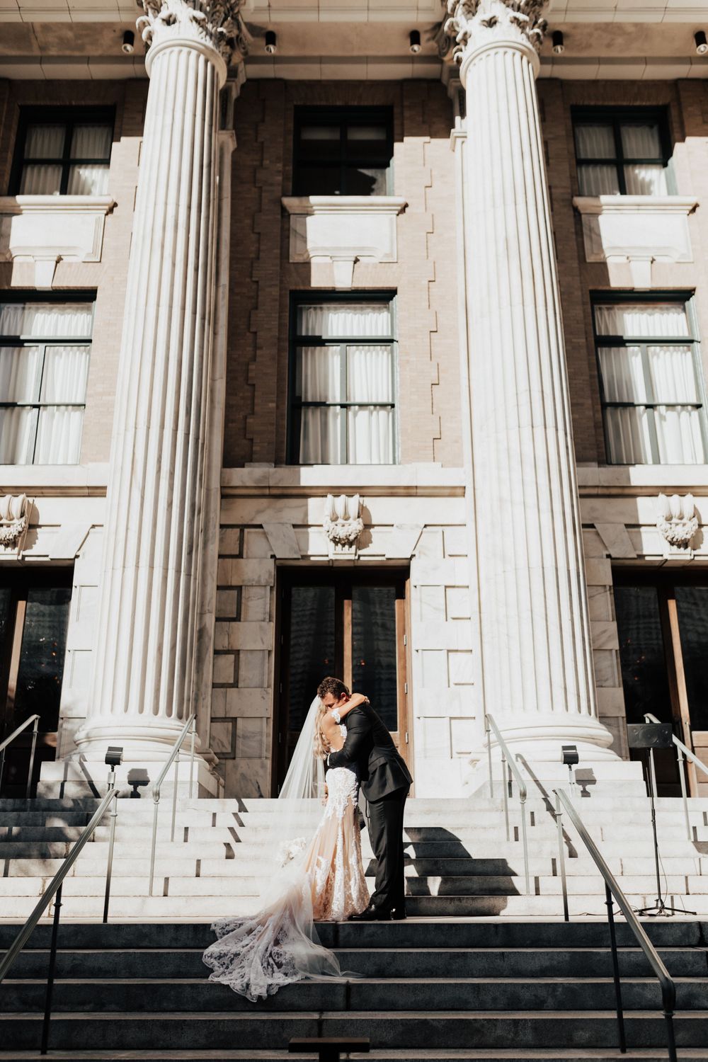 A romantic wedding moment captured on marble steps between tall classical columns.