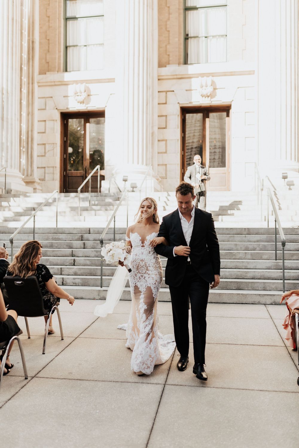 A couple exits their wedding ceremony through classic stone columns and down white marble steps.
