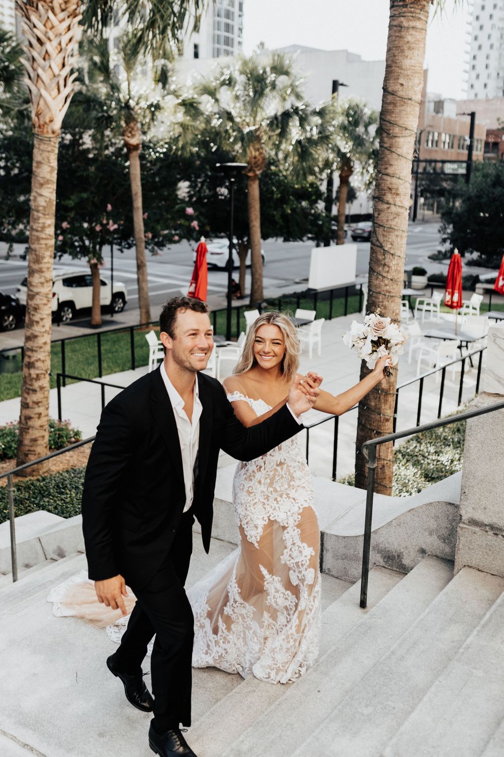 A couple dances and celebrates on outdoor stone steps surrounded by palm trees.