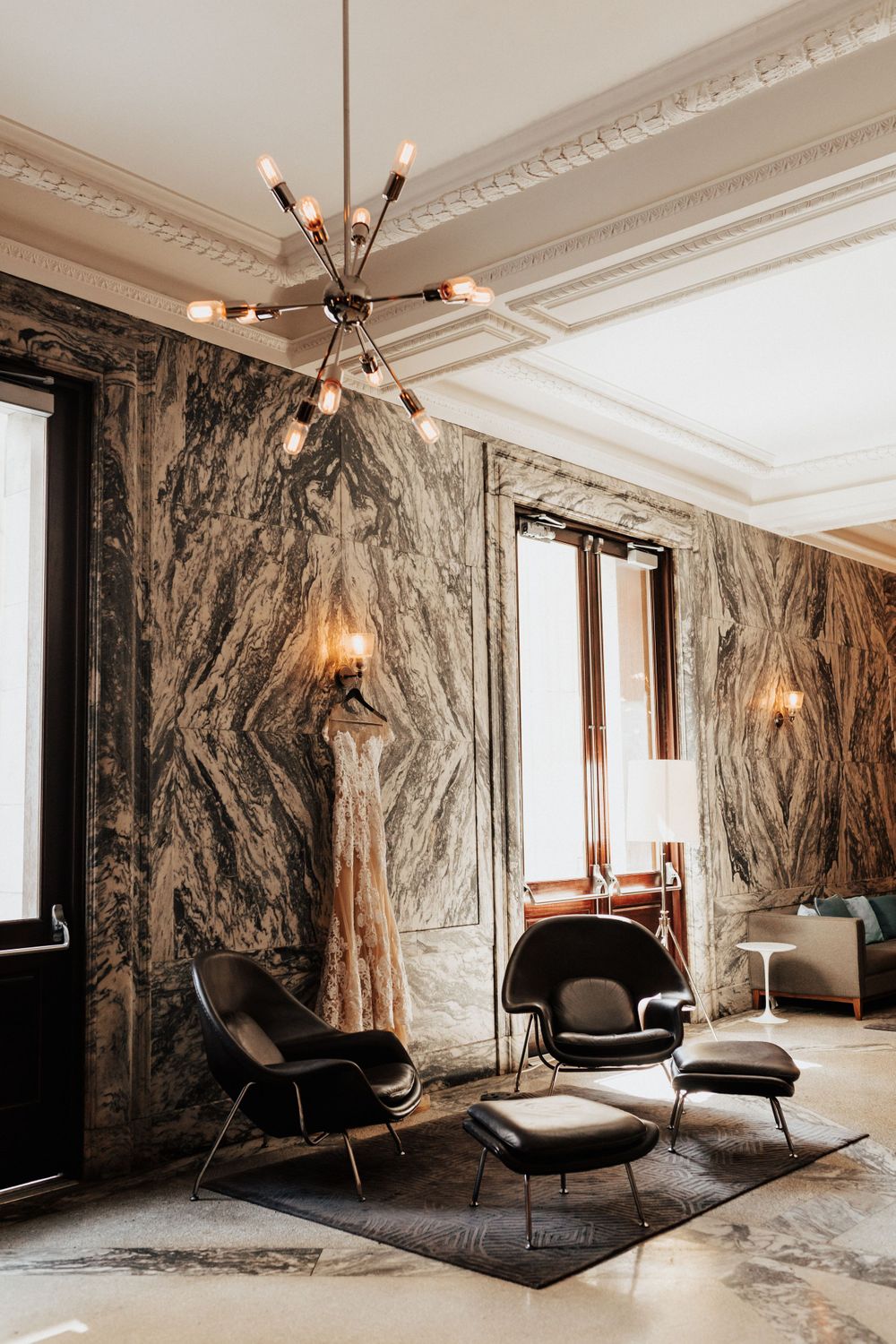 Modern living room with marble walls, sputnik chandelier, and black leather lounge chairs on grey rug.