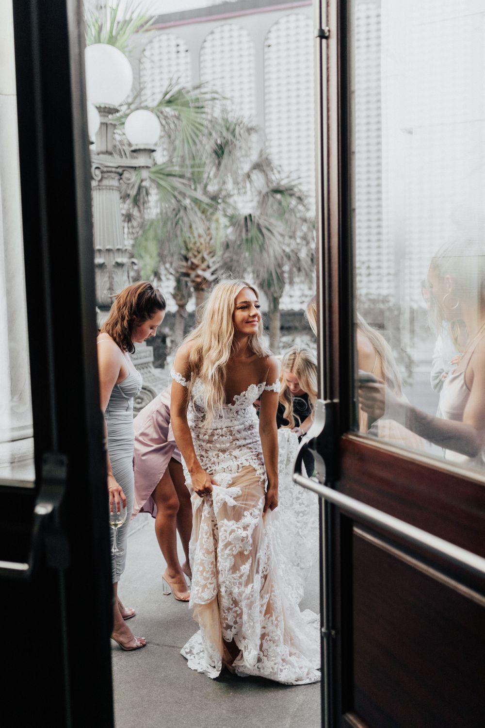 A bridal party entering through a doorway with palm trees visible outside.