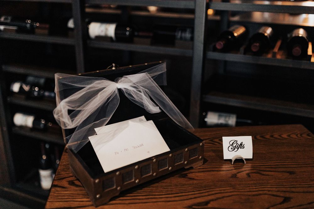 A decorative gift box with ribbon sits on a wooden surface near wine storage.