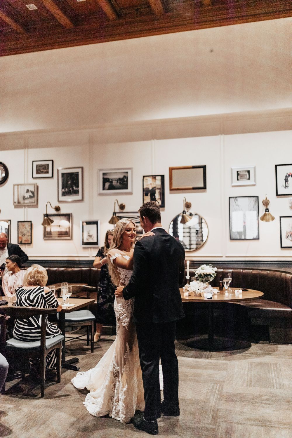 A couple shares an intimate dance moment in a restaurant with vintage photos adorning the walls.