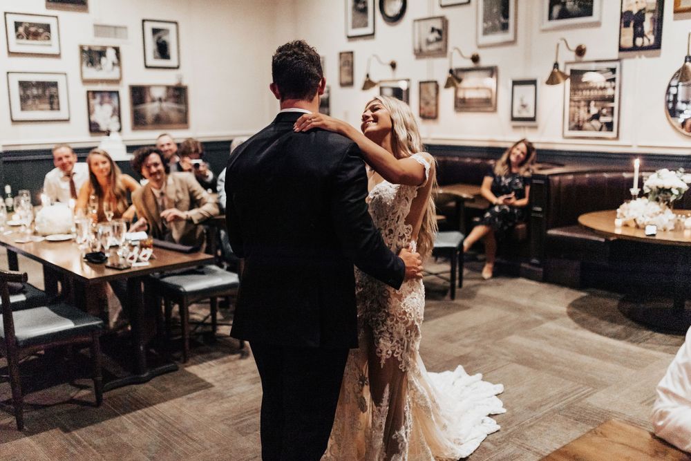 A couple dancing in a cozy restaurant while guests watch from nearby tables.