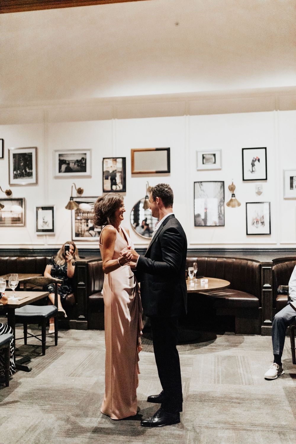 A couple shares an intimate dance in a vintage-styled restaurant with framed photographs on the walls.