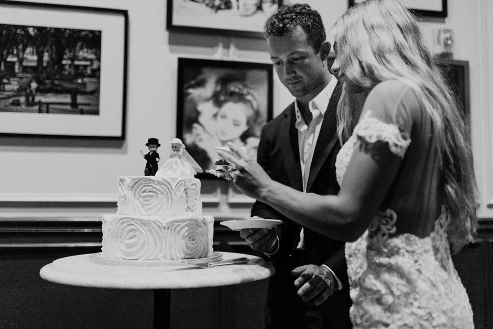 A couple admires their white wedding cake decorated with elegant swirls in a restaurant setting.
