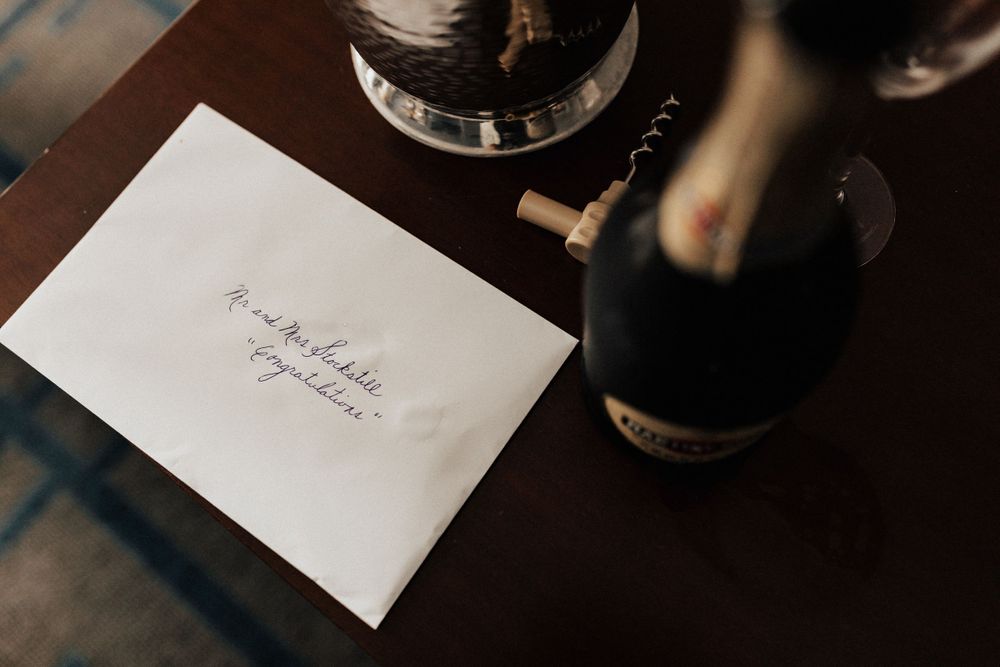 Wedding invitation and wine bottle on dark wooden table with moody lighting.
