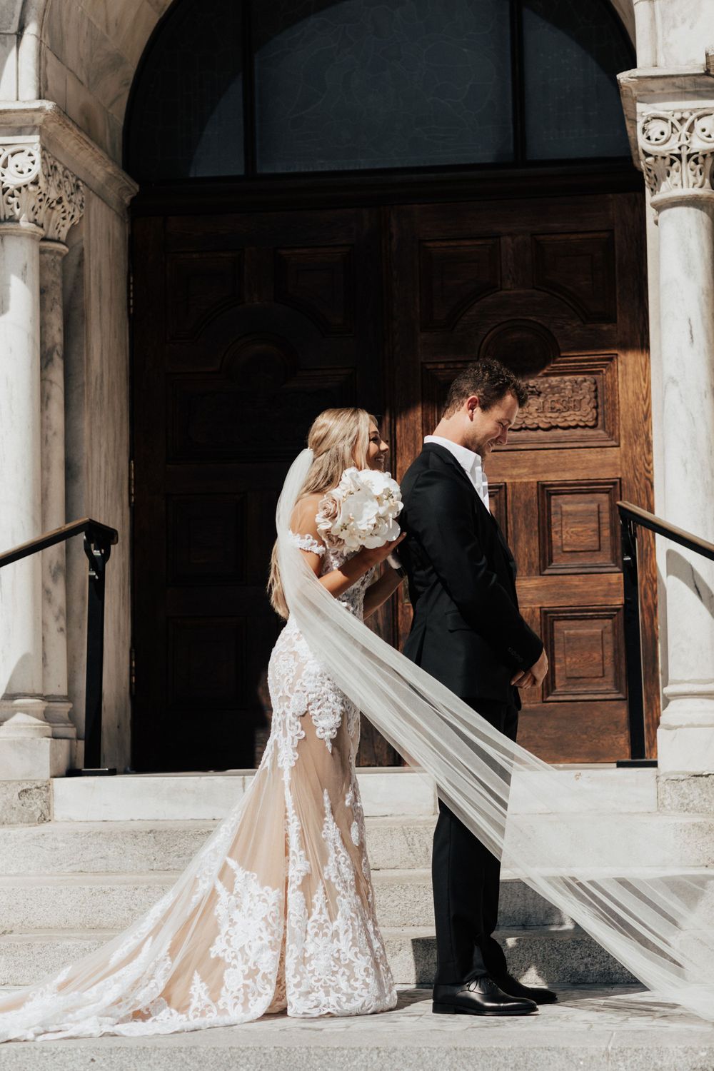 A romantic wedding moment captured in front of an elegant wooden church door with white stone columns.