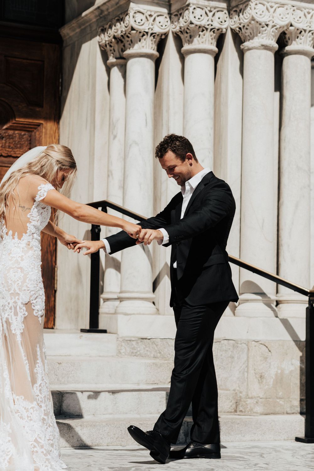 A couple sharing a romantic first look moment on stone steps with ornate architectural columns in the background.
