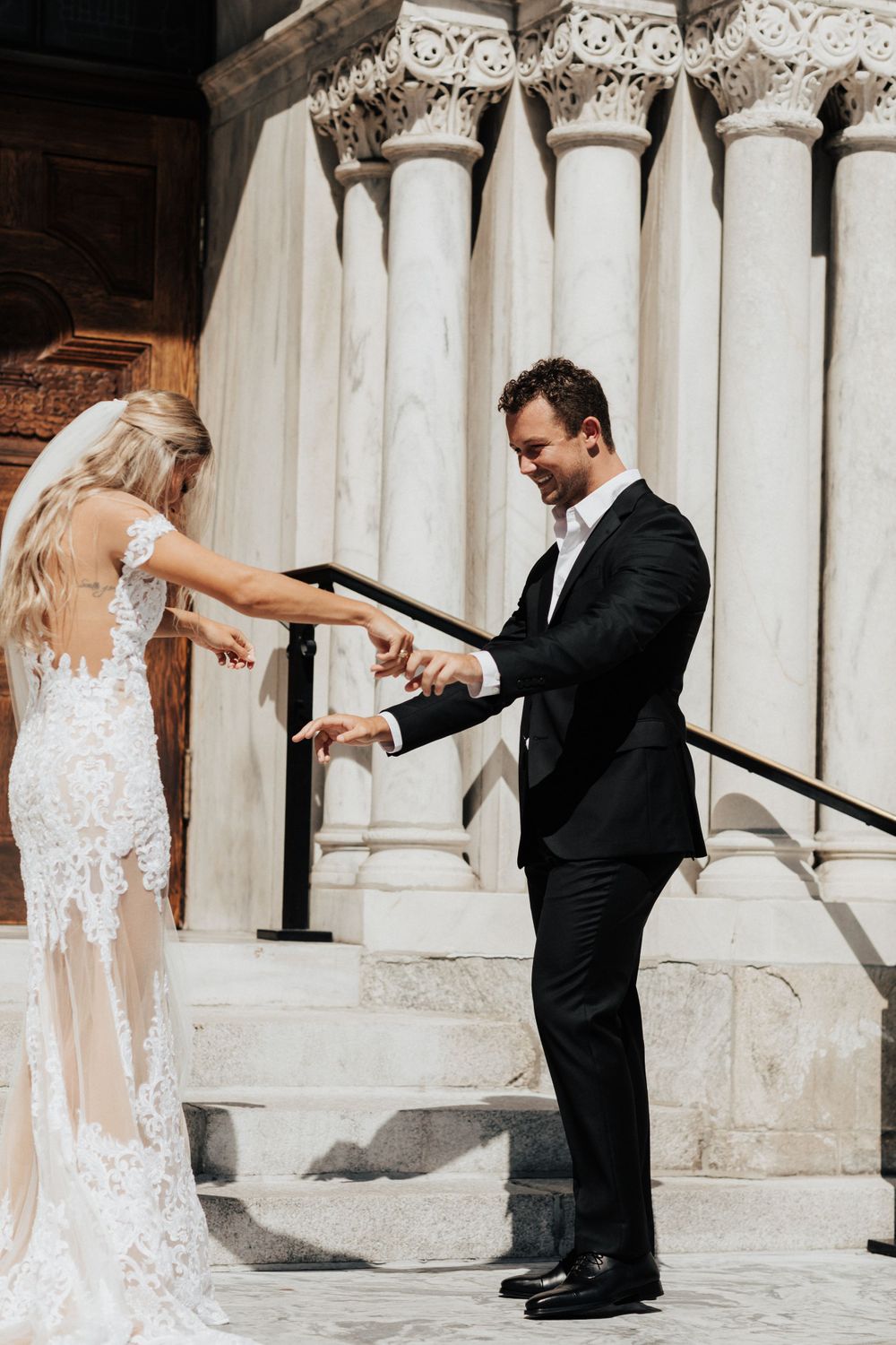 A beautiful couple having a sweet interaction on church steps with classic white stone columns.