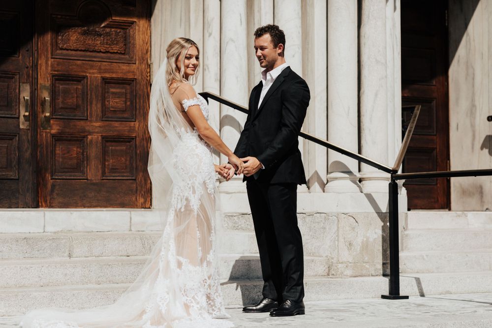 A wedding couple stands together on stone church steps holding hands in an intimate moment.