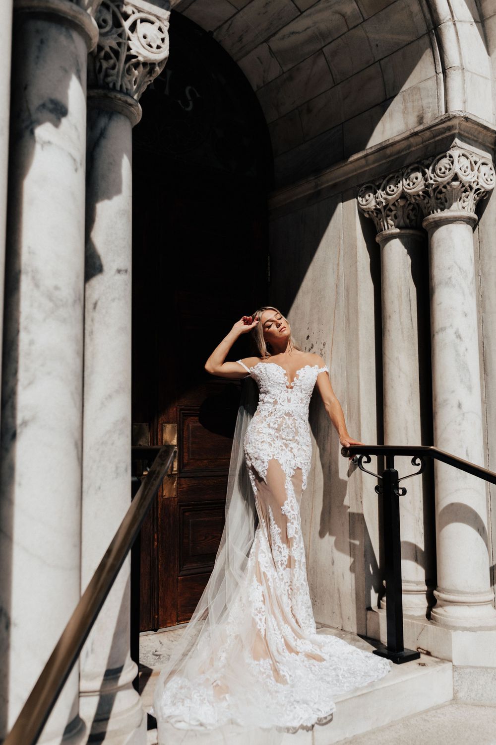 A stunning lace wedding dress with sheer details photographed against classic stone architecture.