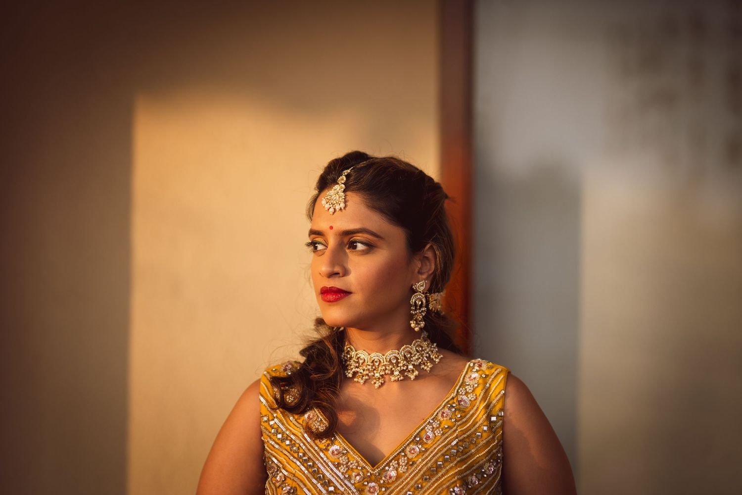 A traditional Indian bride wears an ornate gold lehenga and statement jewelry in warm lighting.