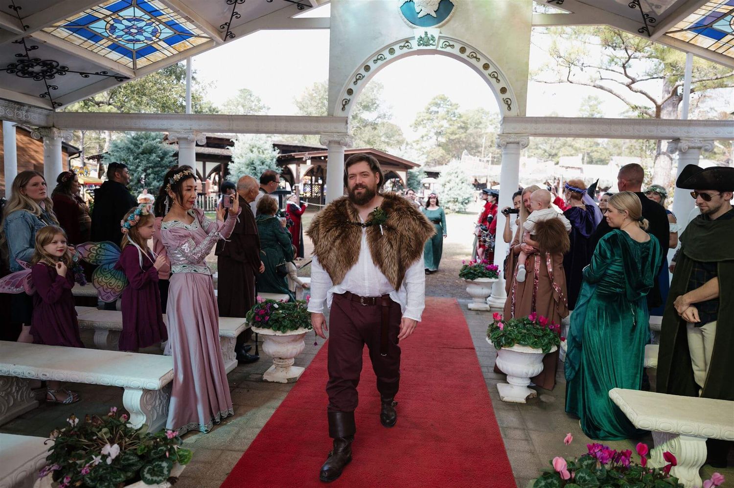 Performers in period costumes walk down a red carpet during a medieval-themed celebration.