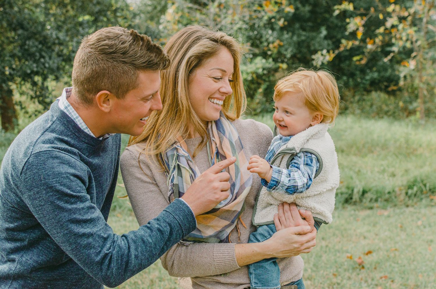 a couple smiles at their one year old son in their arms