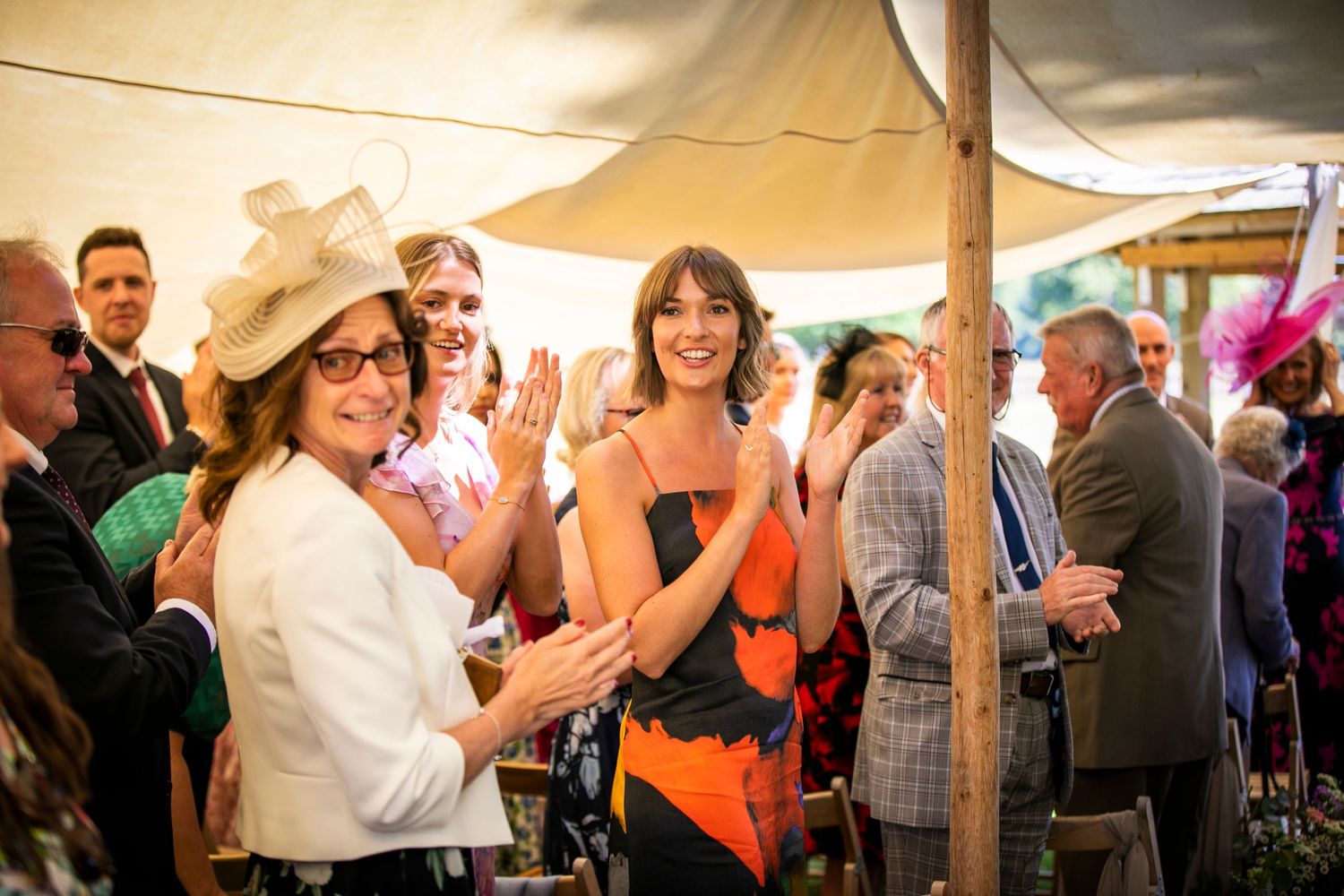 Wedding reception guests dancing and celebrating under a tent with warm lighting.