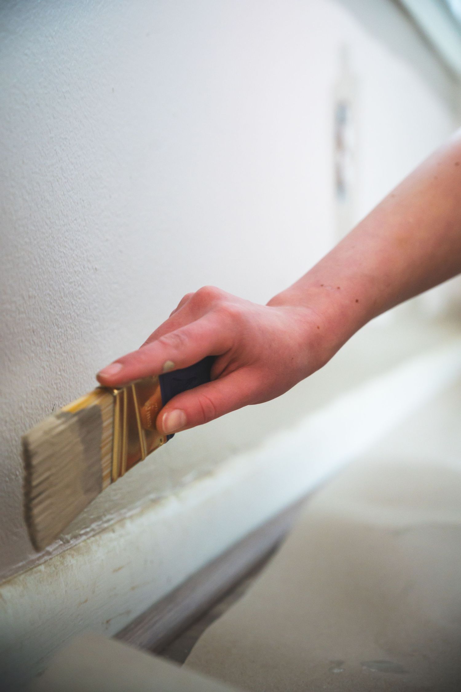 Close-up of a hand holding a paintbrush against a white wall during painting.