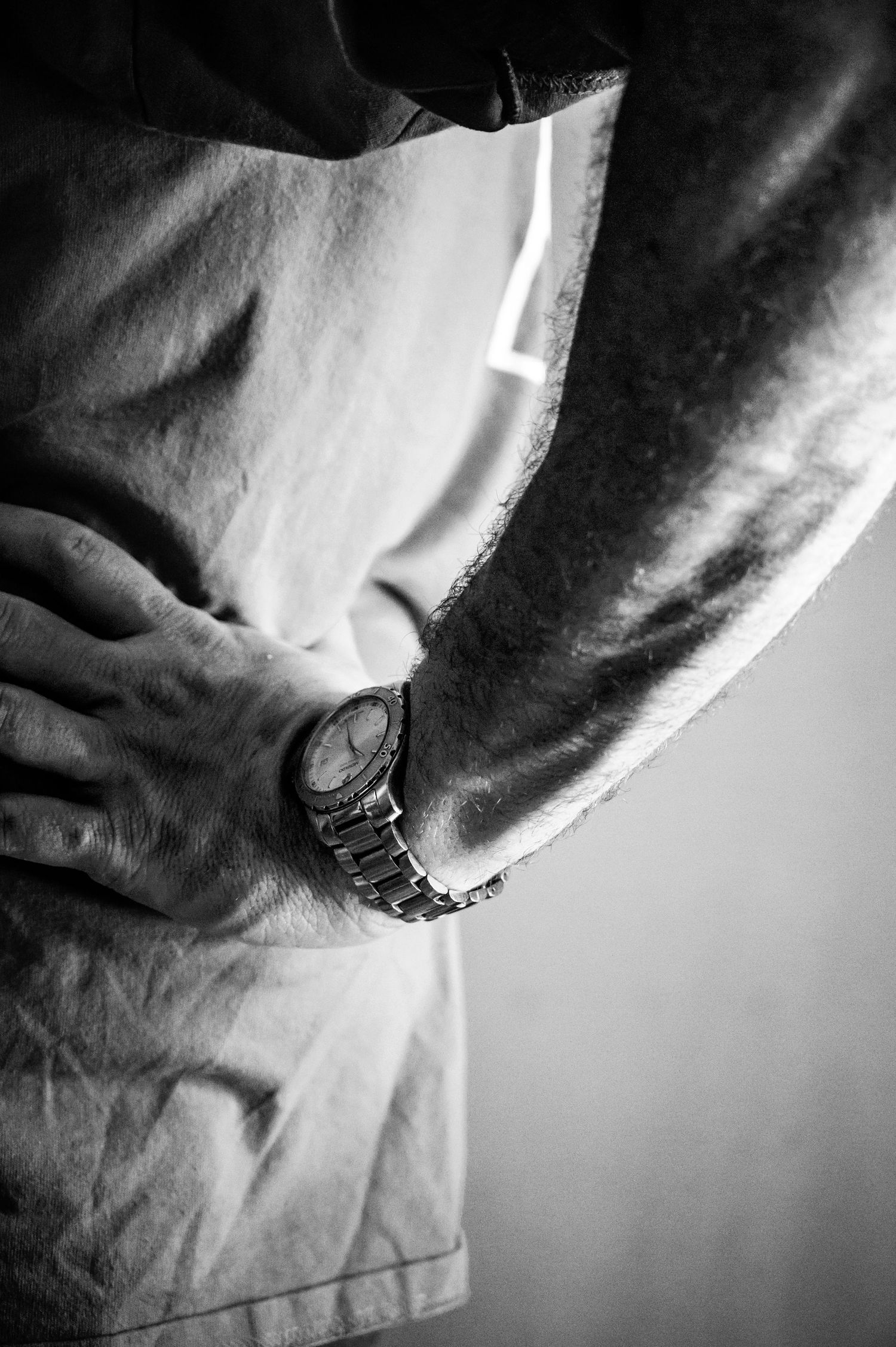 Black and white close-up of person wearing watch and work clothes.