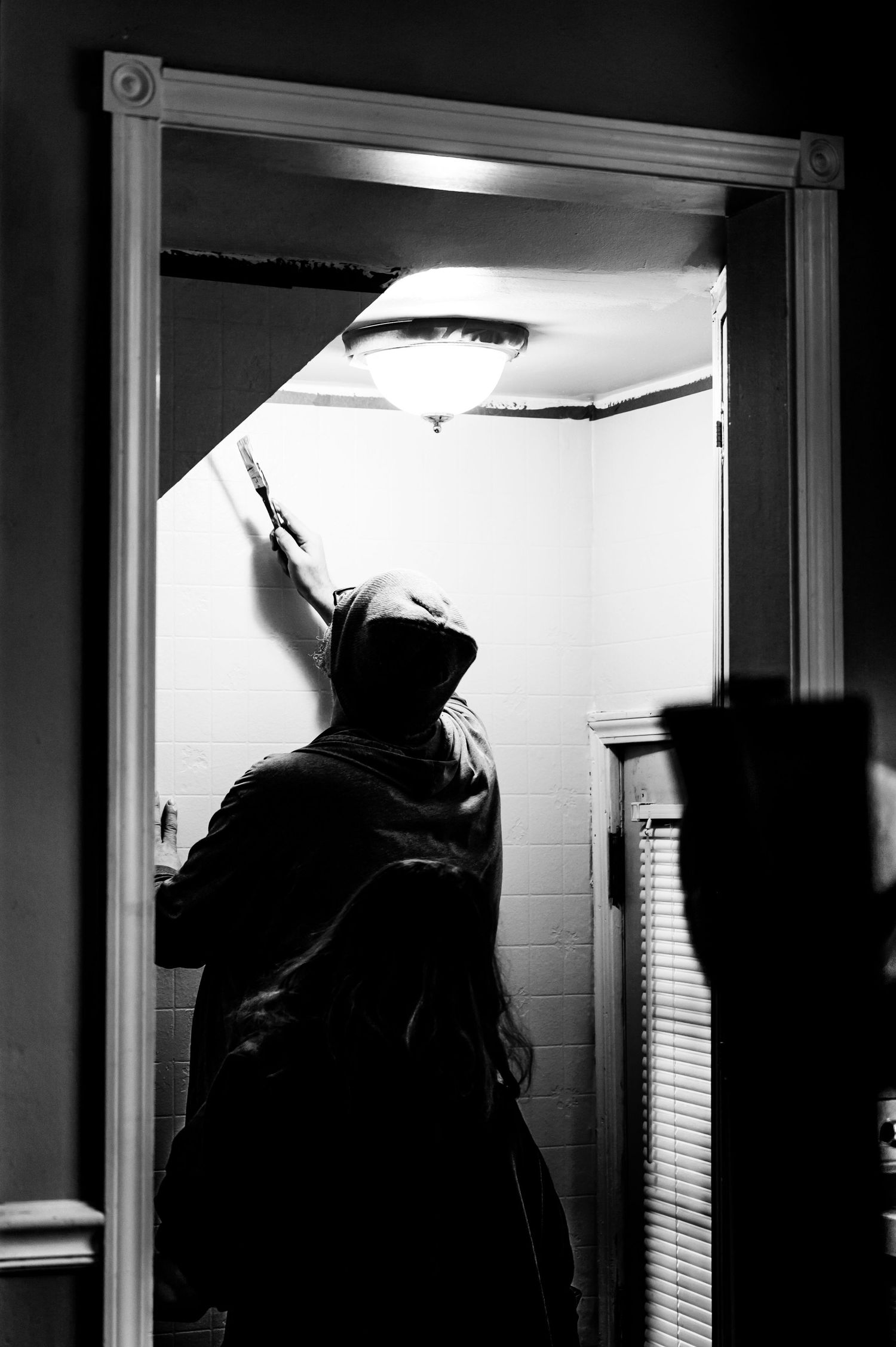 Silhouette of person painting a ceiling in a doorway with dramatic lighting.