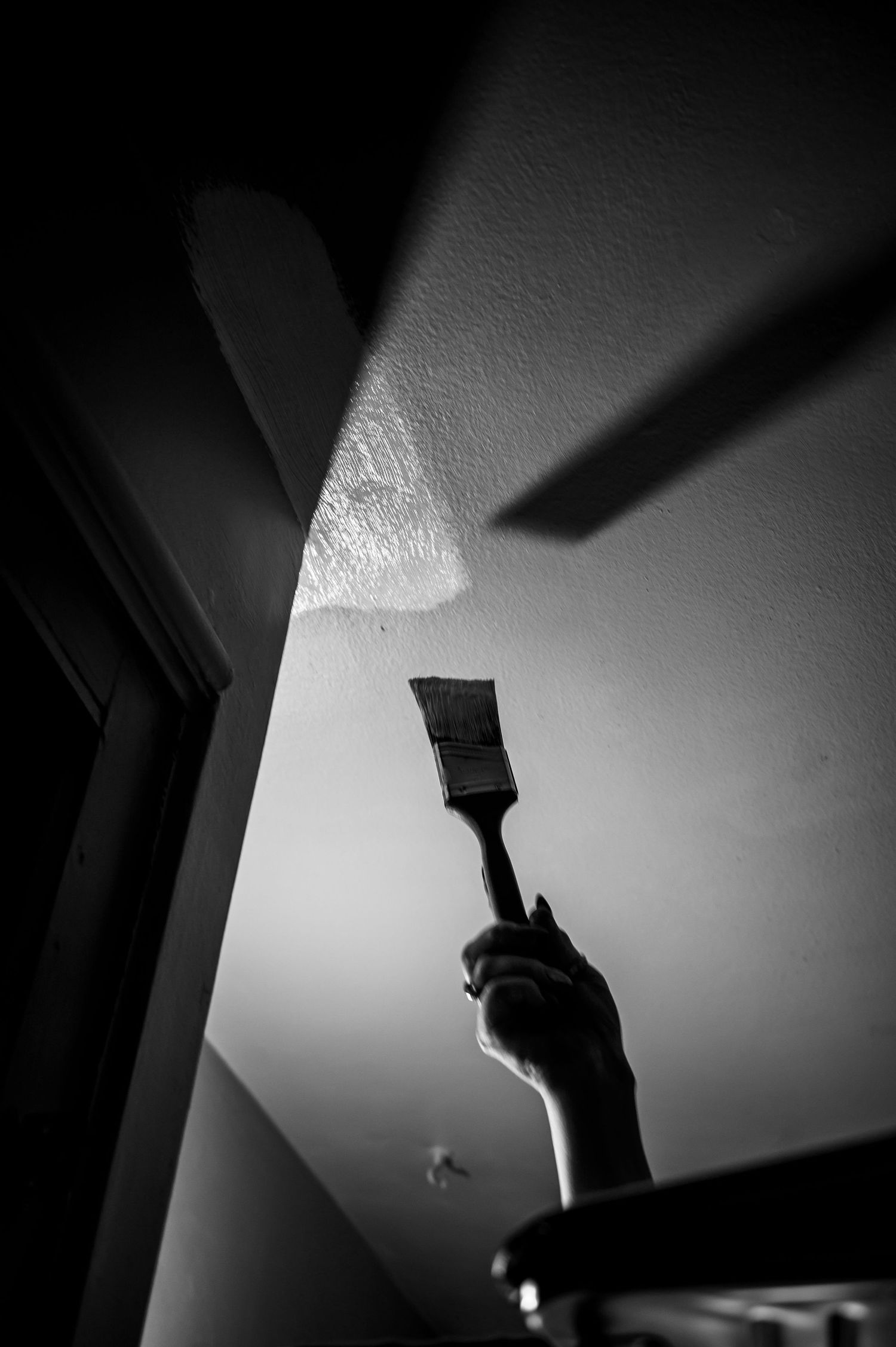 Dramatic black and white shot of hand holding paintbrush against ceiling.