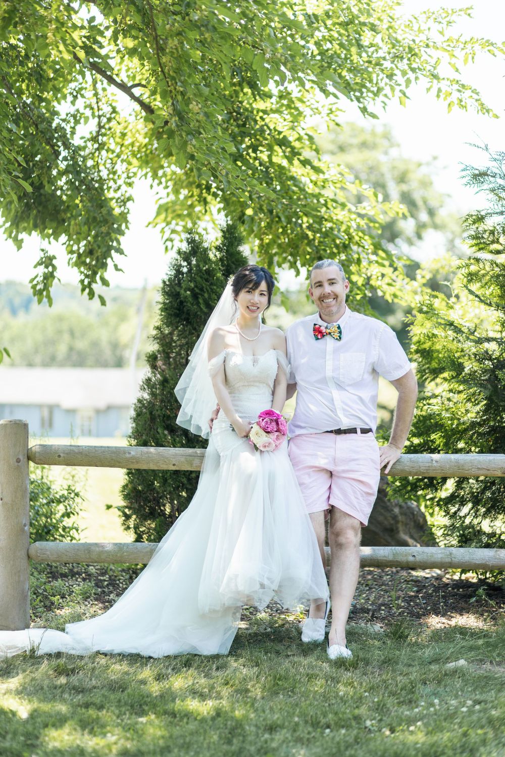 Wedding couple shares tender moments on a grassy hillside with rustic fence backdrop.