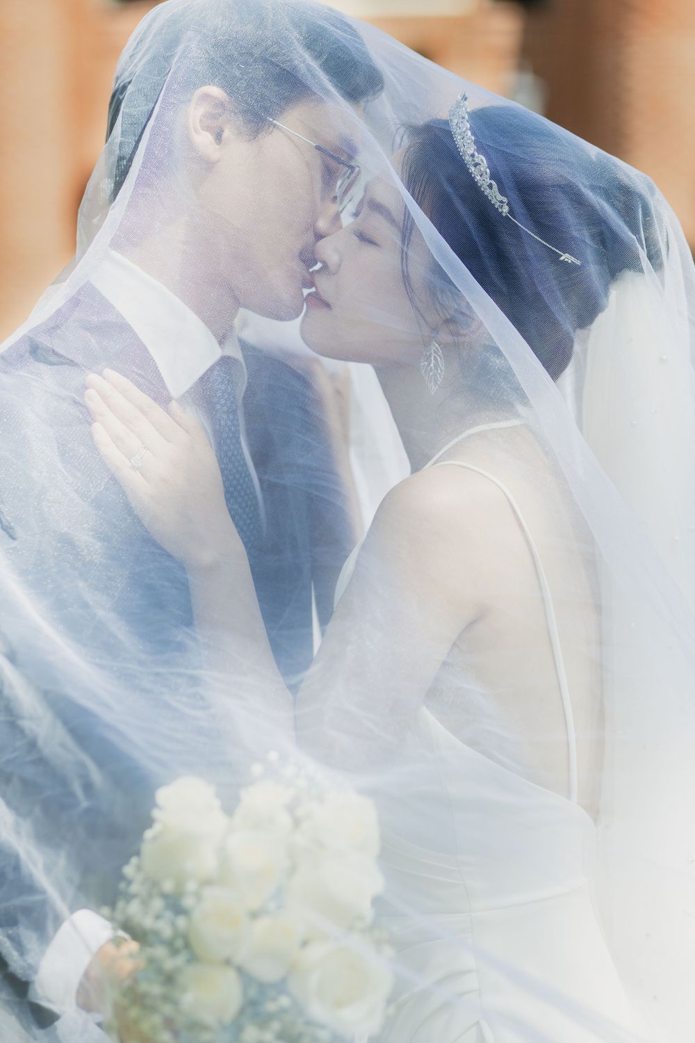 Romantic wedding portrait with couple sharing intimate moment under white veil.