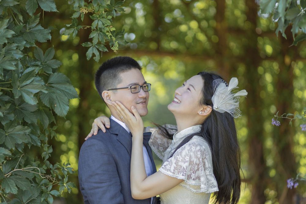Joyful wedding couple sharing a tender moment under green foliage.
