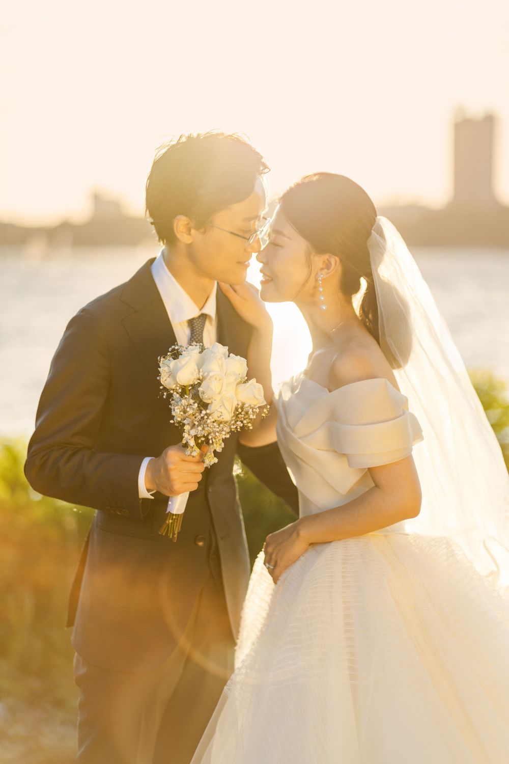 Sunset wedding portrait with golden light and waterfront cityscape in background.
