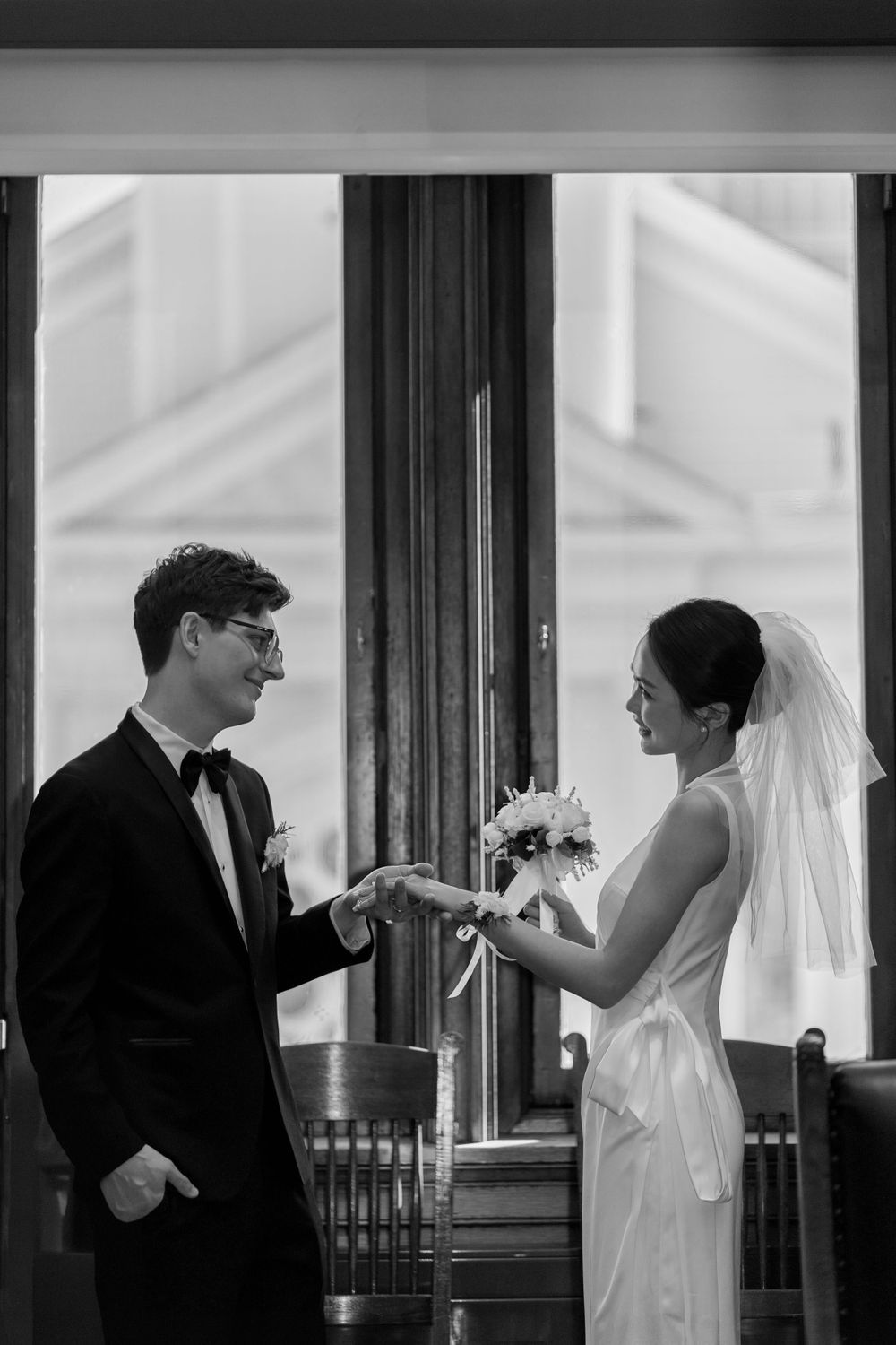 A black and white wedding photo of a couple exchanging rings in a traditional ceremony.