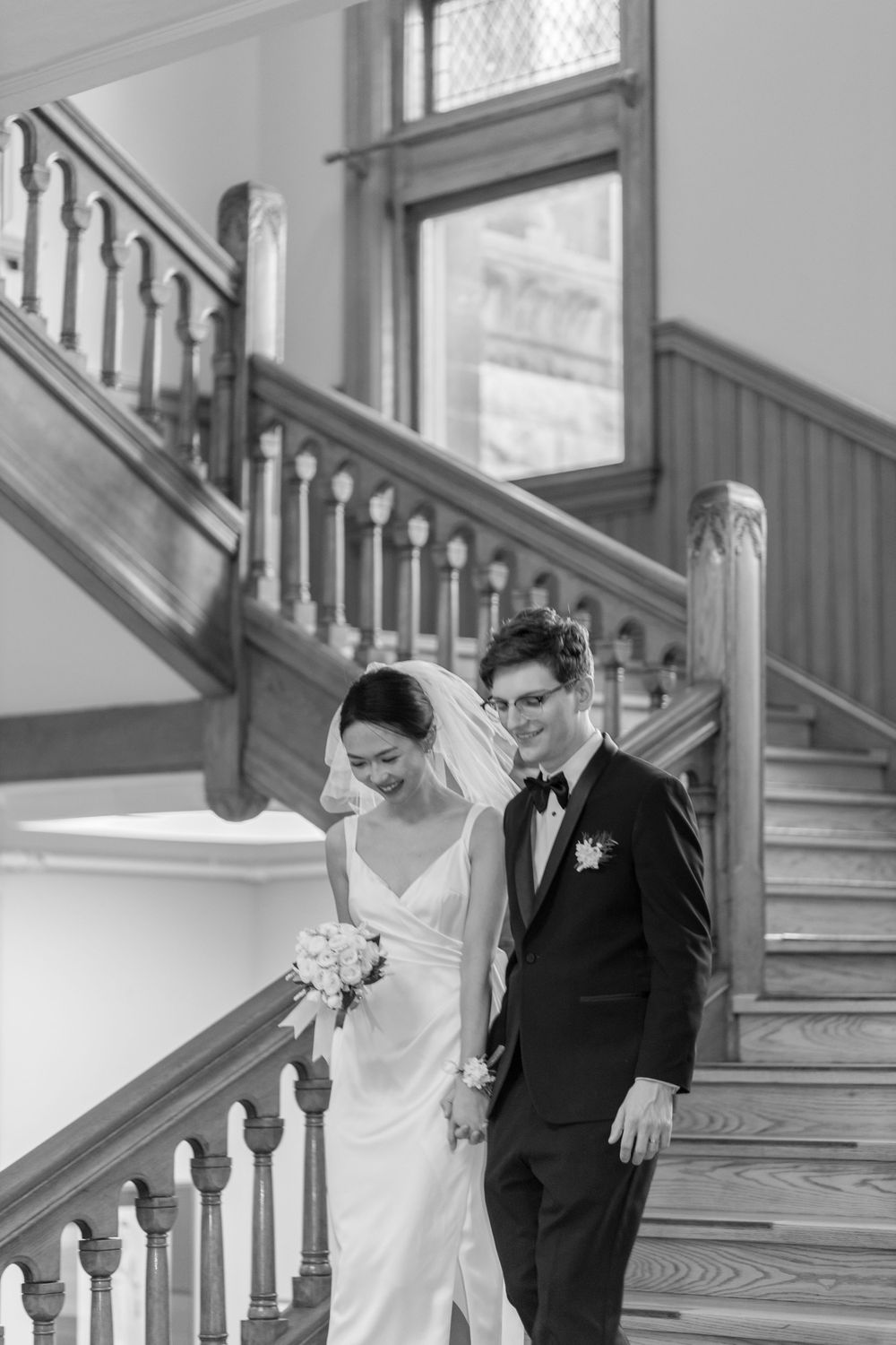 A black and white photo of newlyweds descending a grand wooden staircase.