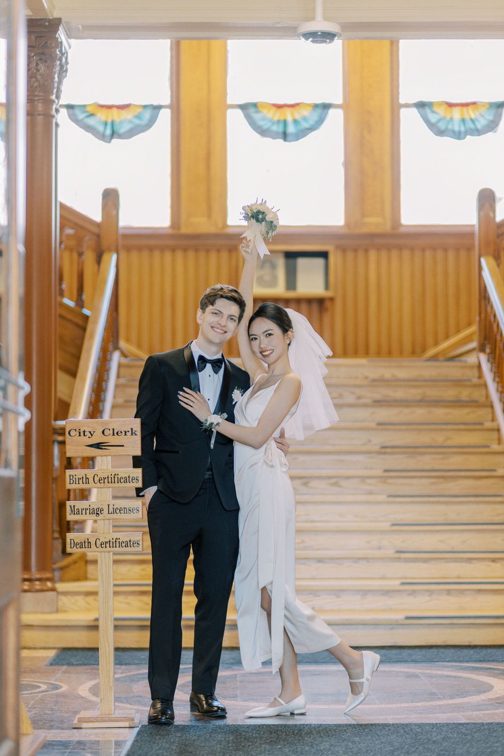 A wedding couple posing at the bottom of a staircase with decorative fan bunting overhead.