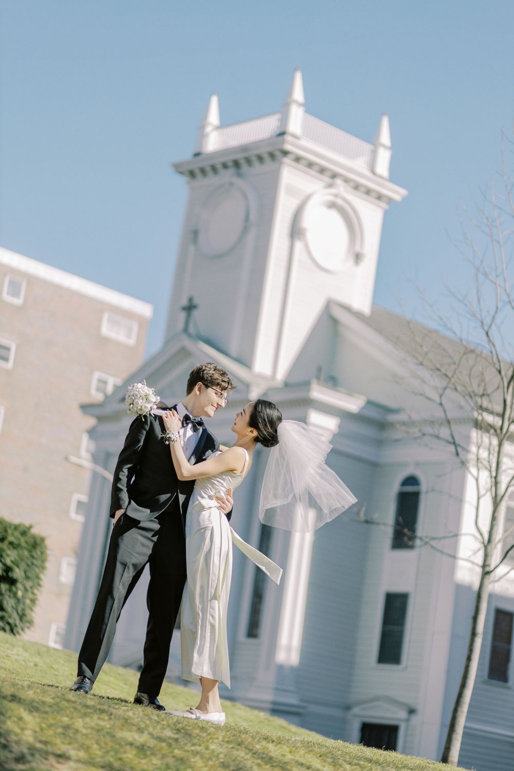 A white church serves as backdrop for a romantic wedding photography session in natural light.
