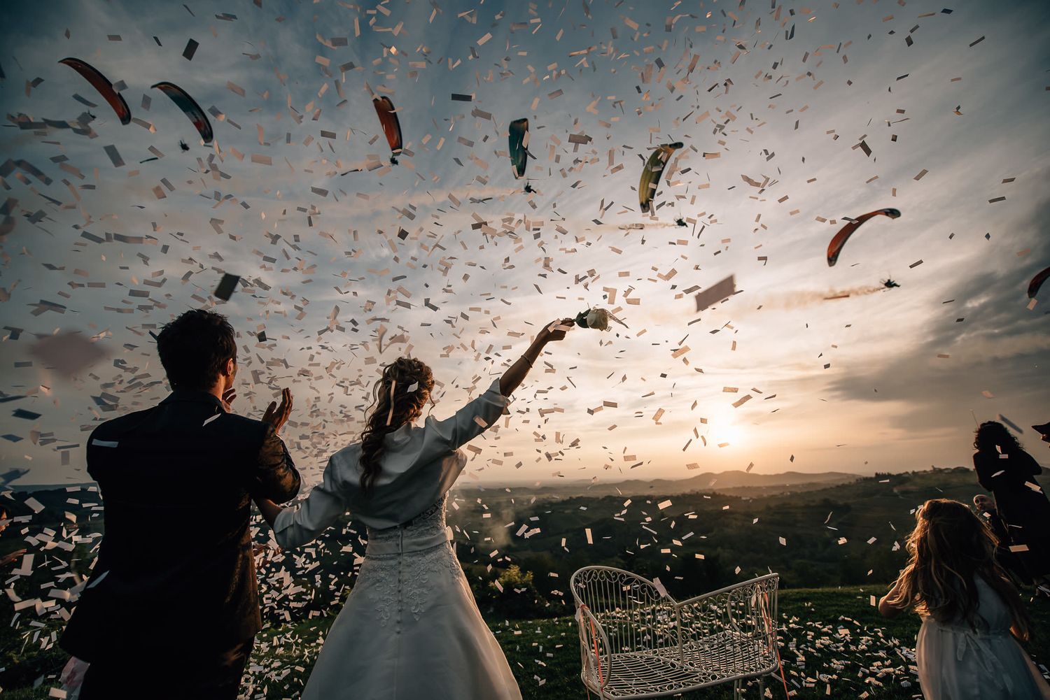 Confetti fills the sunset sky as wedding guests celebrate outdoors.