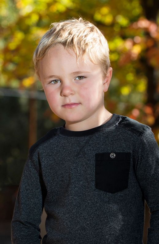 Portrait of young person in dark shirt with blonde hair against autumn foliage.