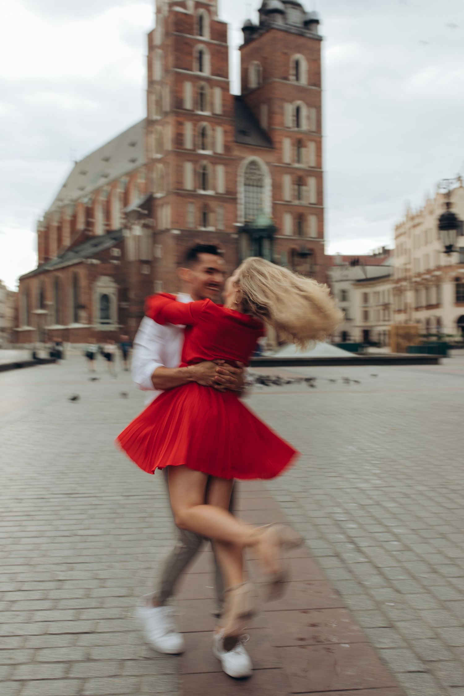Dancing couple in red attire spinning in front of historic church building in town square.