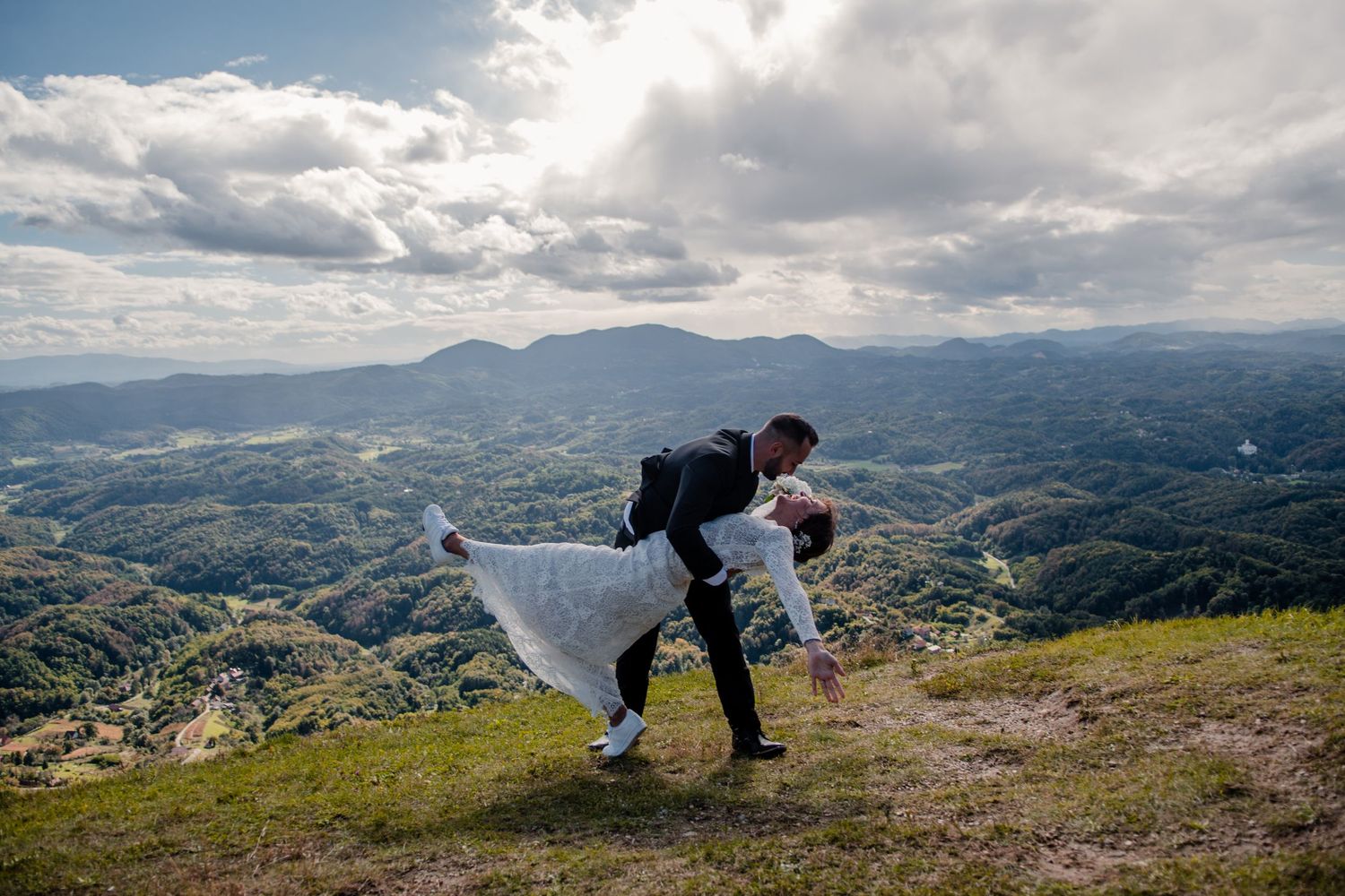 A dramatic mountaintop wedding photo with sweeping valley views and cloudy skies.