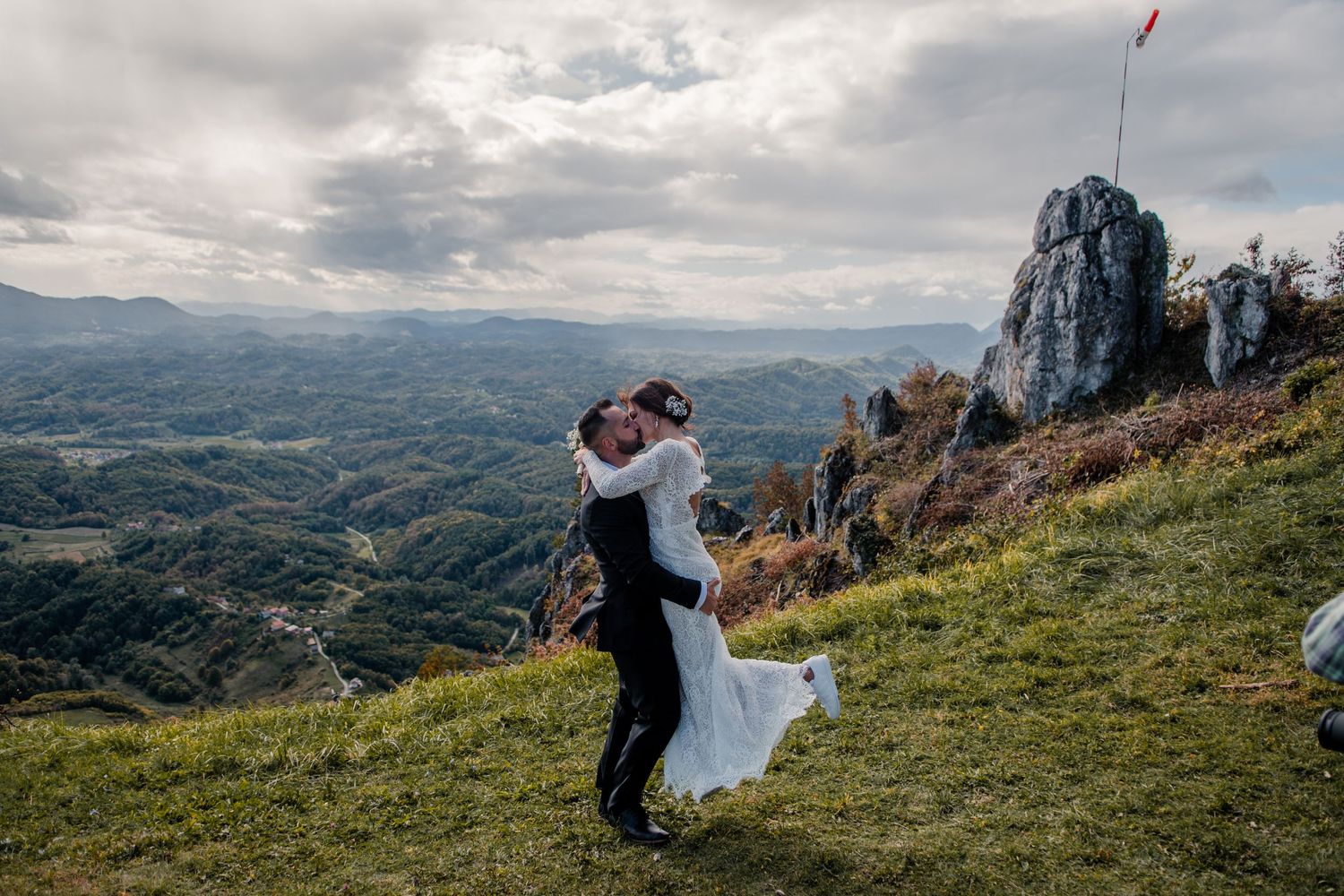 A romantic embrace on a mountain peak with dramatic landscape and cloudy skies in the background.