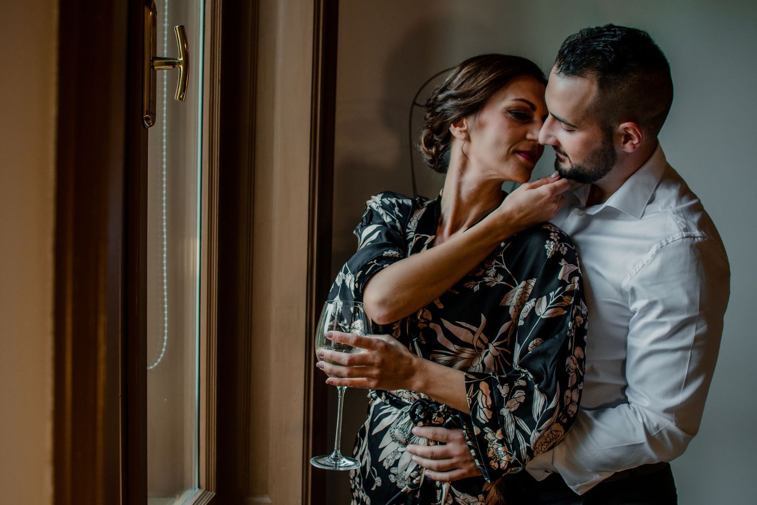 Romantic couple in an intimate moment sharing champagne by a window.