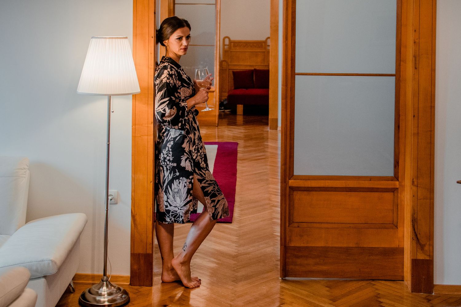 Person in a floral dress standing by a vintage lamp and wooden doorway.