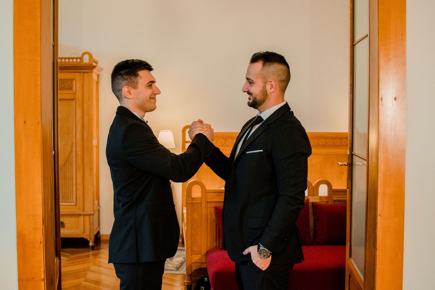 Two men in suits sharing a celebratory handshake indoors.