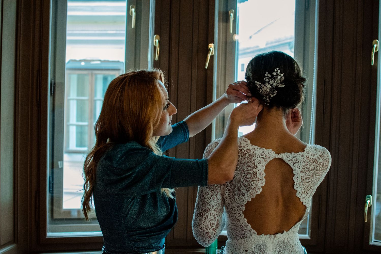 Final adjustments being made to bridal hair and dress near a window.