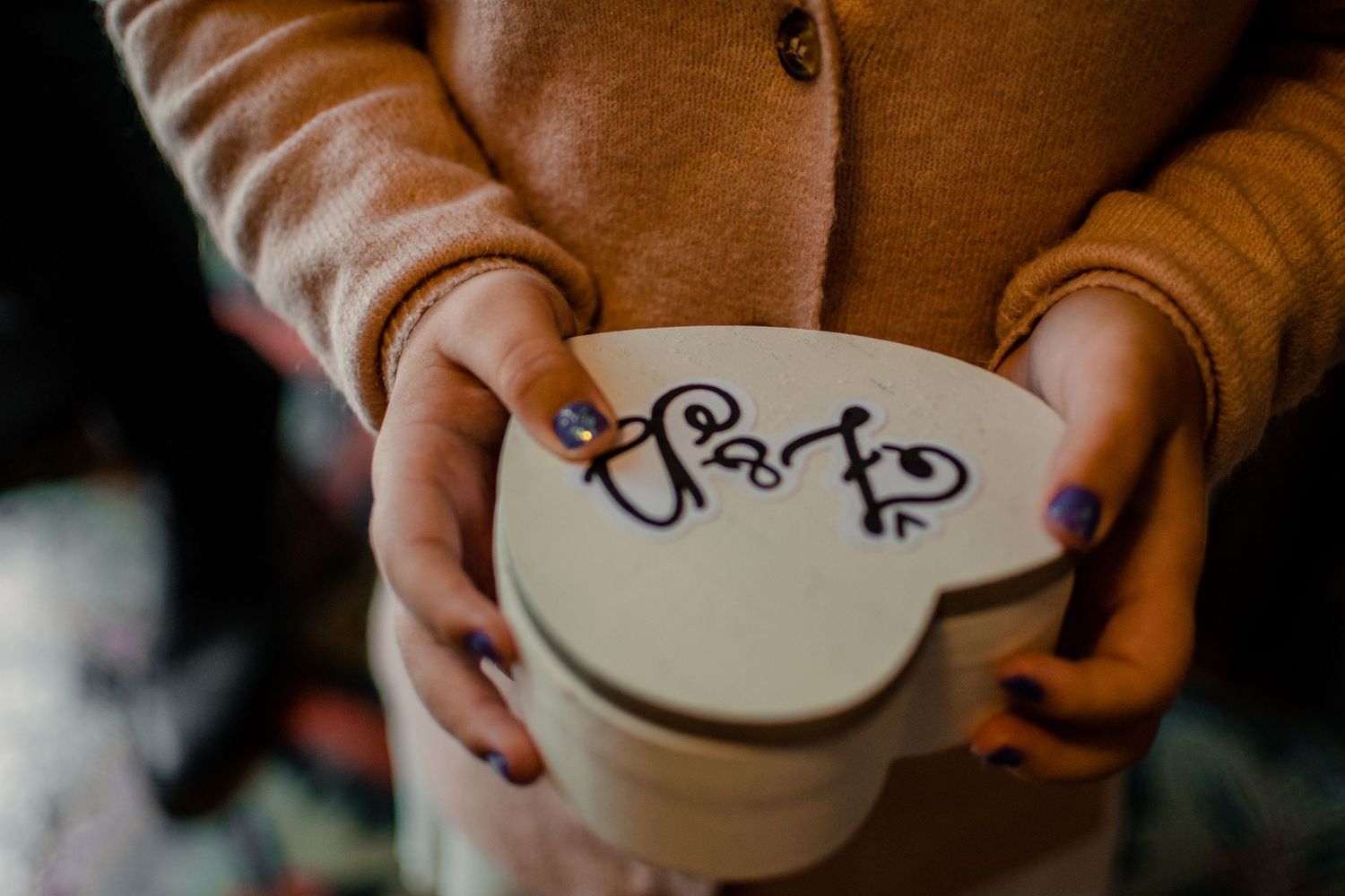 Hands holding a white heart-shaped box with decorative text.