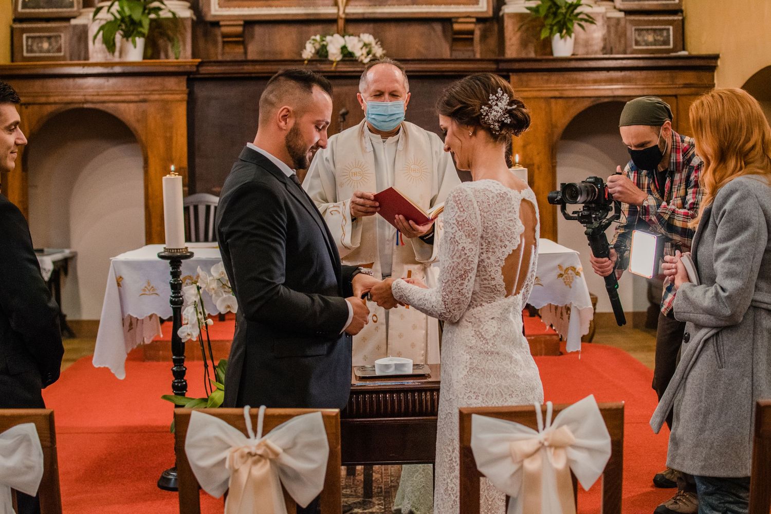 Indoor wedding ceremony with decorative white bows and floral arrangements in an ornate venue.