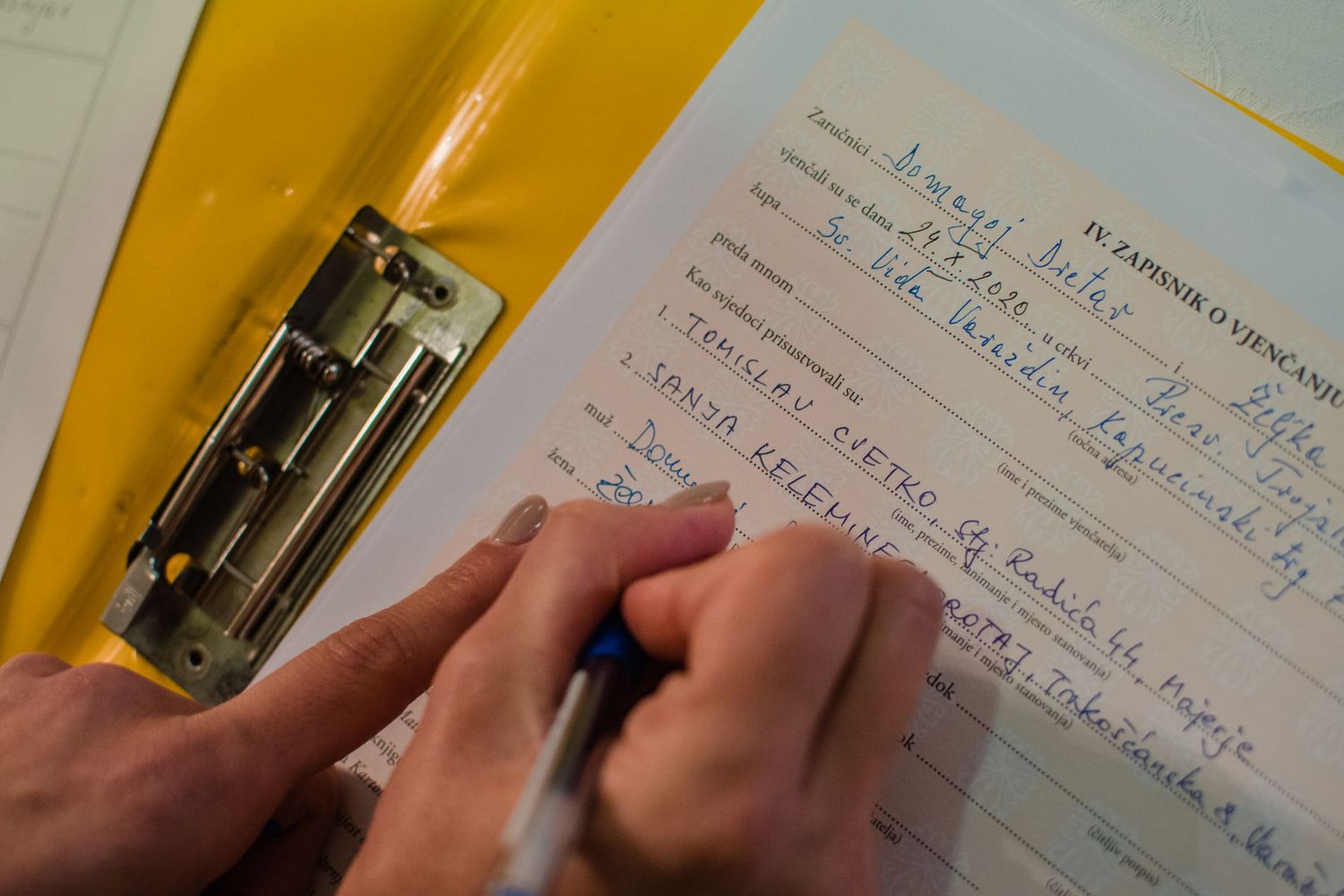 A hand writes notes in a journal with a yellow folder nearby.