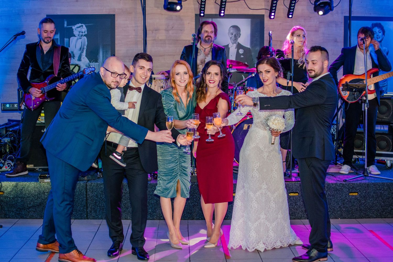 Wedding celebration with live band and group of people posing together under blue lighting.