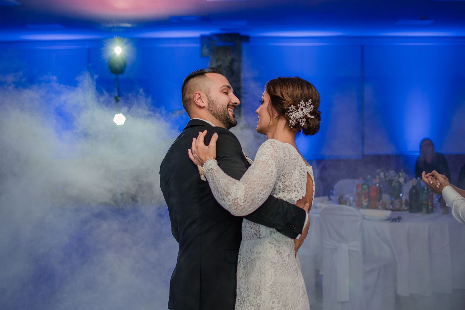 Romantic first dance moment with atmospheric fog and blue lighting at wedding reception.