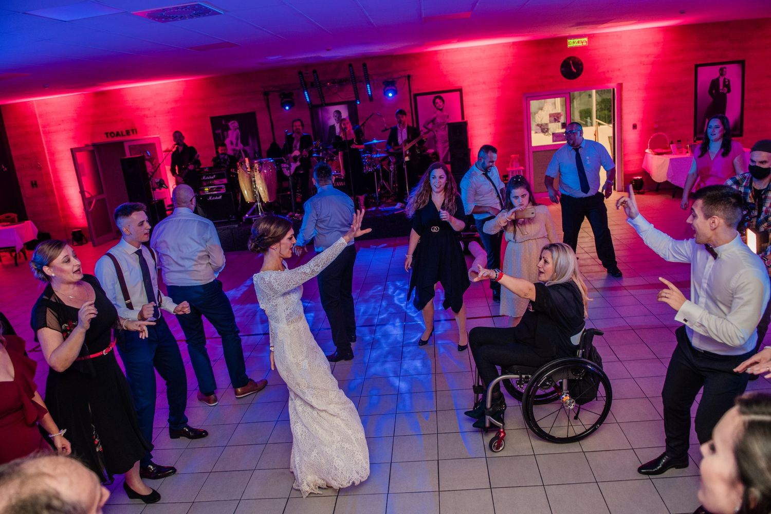 Wedding reception dance floor with guests dancing under vibrant red and purple lighting.