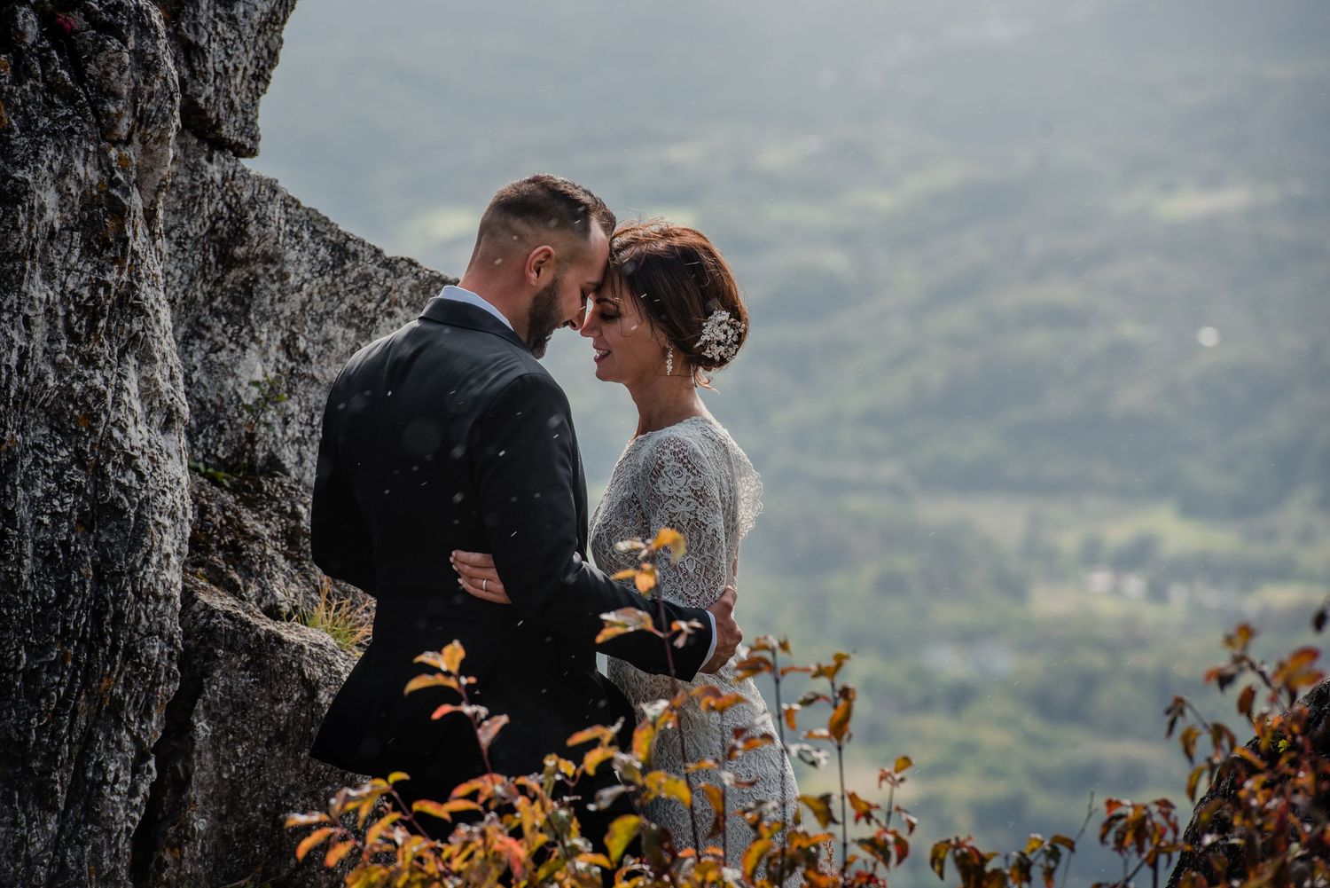 Intimate moment between newlyweds on rocky mountain ledge surrounded by autumn foliage.