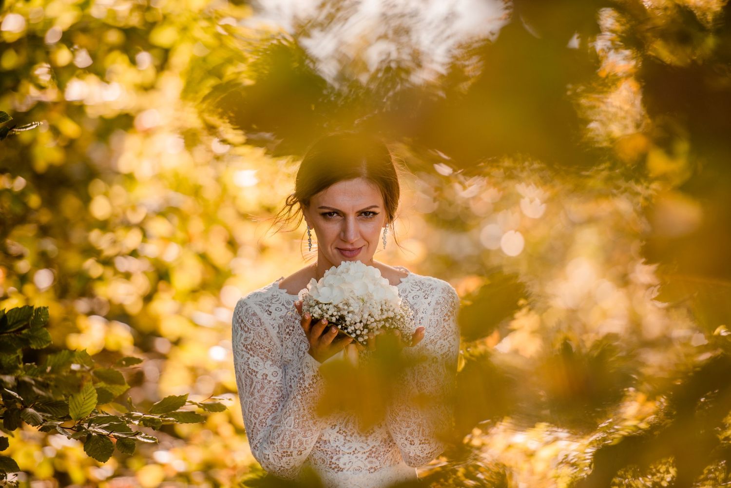 Ethereal portrait of bride in lace dress amid golden autumn foliage.