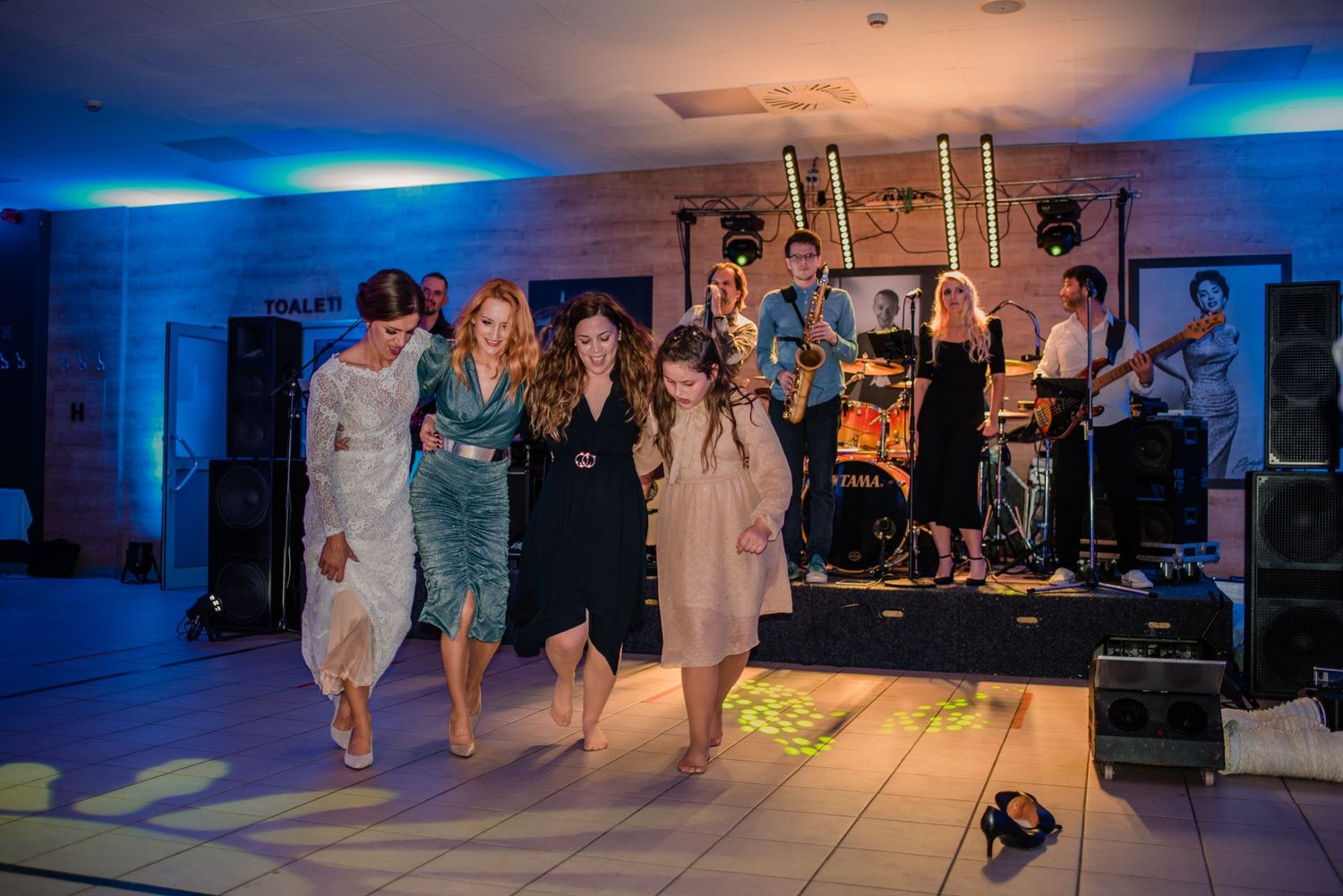 Group of wedding guests dancing together at a reception with a live band performing on stage.